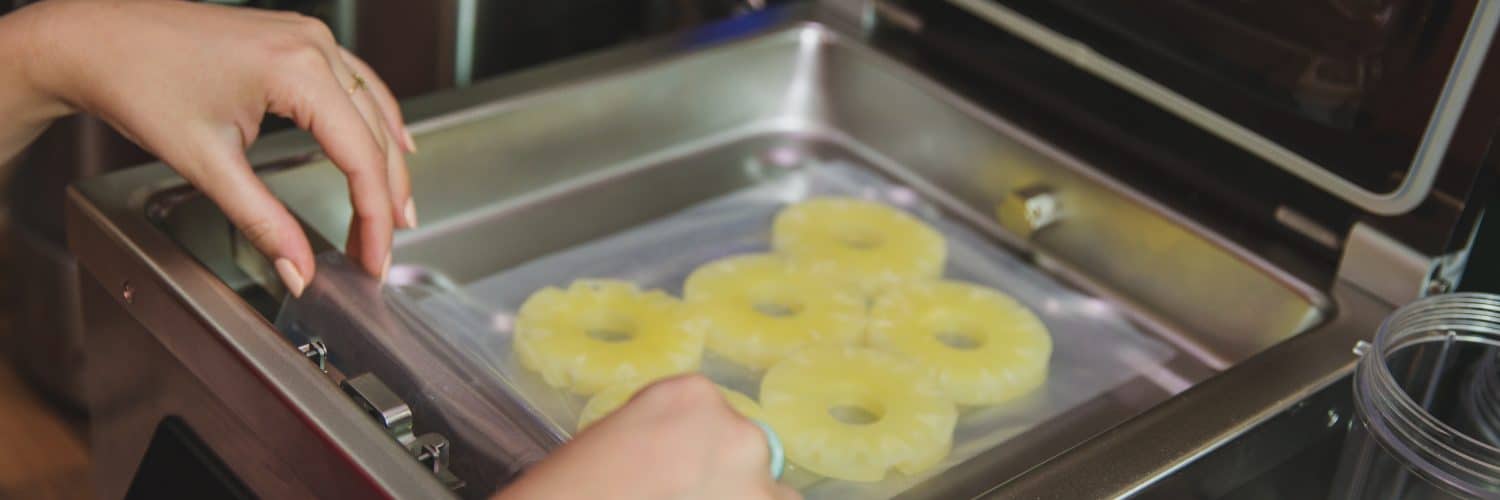 Pineapple slices in a bag, with hands putting them inside a chamber vacuum sealer.