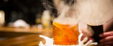 Side view of a cocktail glass being infused with smoke.