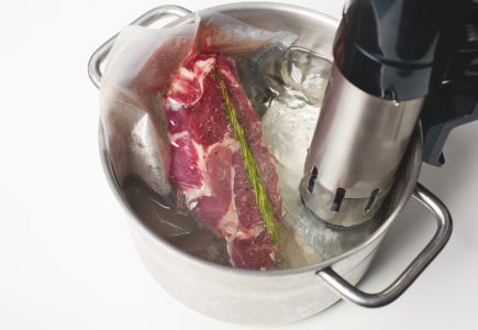 Steak in a vacuum sealed bag inside a large pot full of water, with a sous vide machine next to it.
