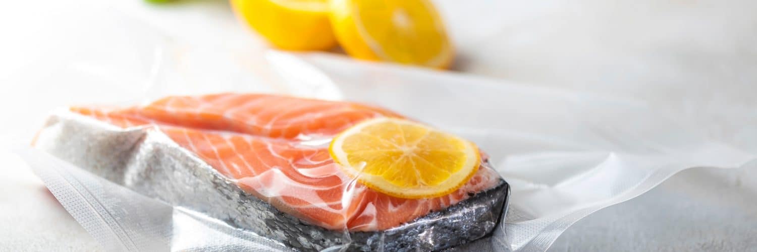 Side view of a vacuum-sealed bag with a cut of fish and lemon.