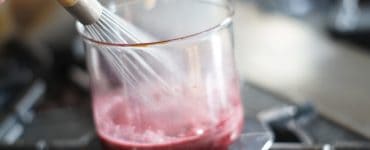 Glass container over a fire with a whisk stirring its contents.