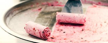 Close up shot of ice cream being rolled out of a freezing plate with a metal spatula.