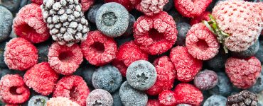 Top view close zoom of several frozen raspberries, strawberries, blueberries, and blackberries.