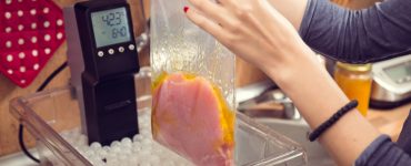 Woman putting vacuum-sealed bag of food into water container with sous vide machine.