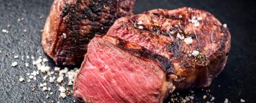 Close-up shot of pink slices of steak on a dark background.