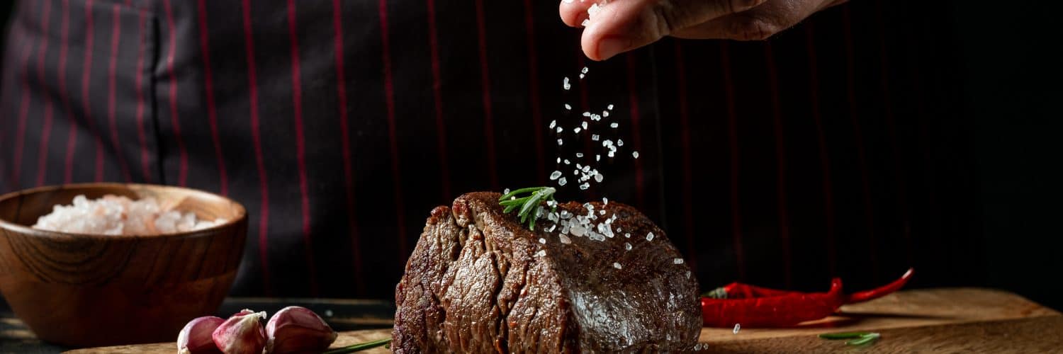 Close up shot of a steak and a chef's hand salting it.