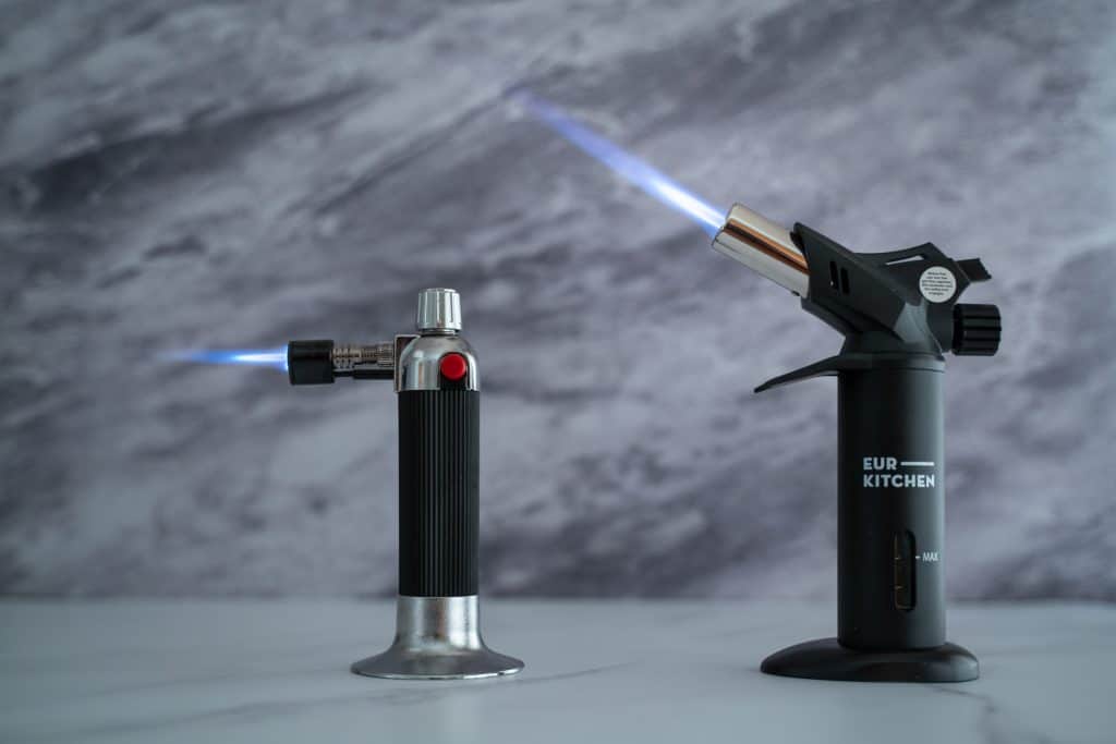 Side view of Eurkitchen torch next to a generic torch showing that the Eurkitchen is bigger and has a considerably bigger flame.