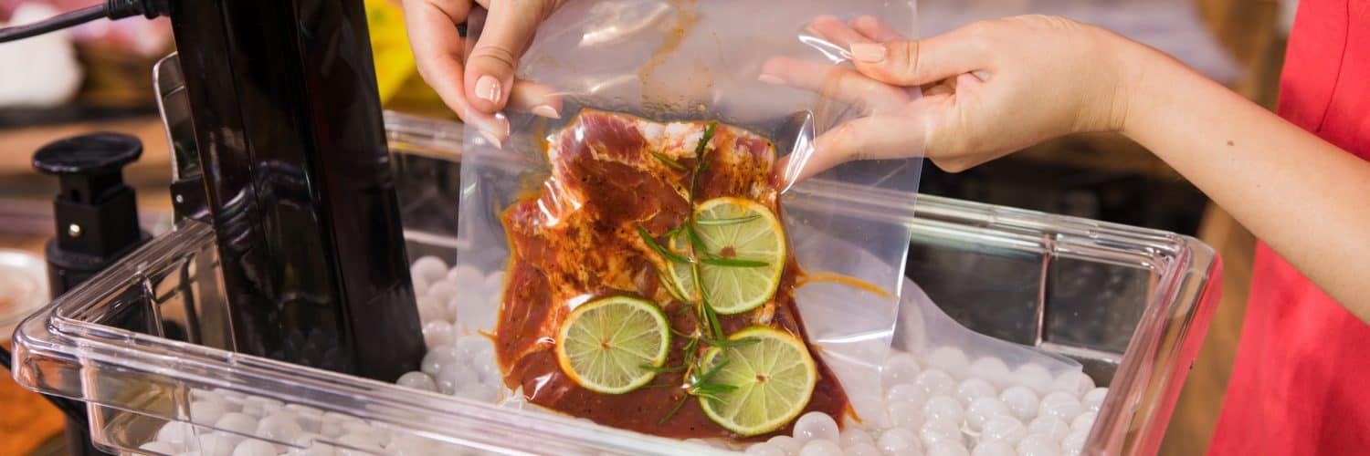 Woman placing vacuum-sealed bag of food into a container full of water and a sous vide machine.