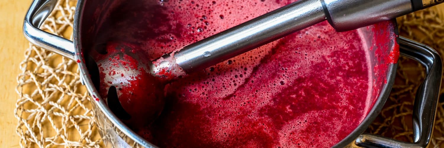 Top view of immersion blender in pot with beetroot soup