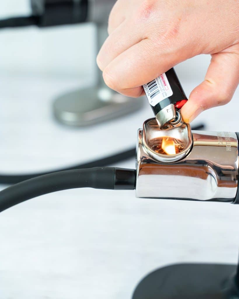 Close-up shot of hand using a lighter to light the PolyScience smoking gun wood chips on fire, with the Breville smoking gun on the background.