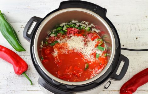Top view of an instant pot with red sauce, rice, onions, and veggies in it.