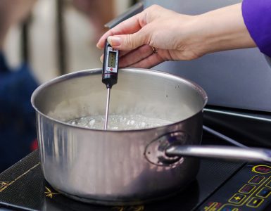 Close-up shot of pan with boiling syrup and a hand holding a thermometer over the pan