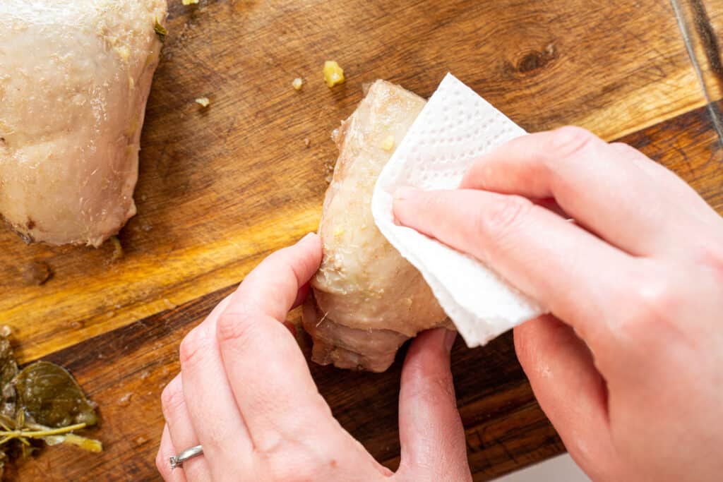 Photo of hands using a paper towel to clean and dry cooked chicken thigh.