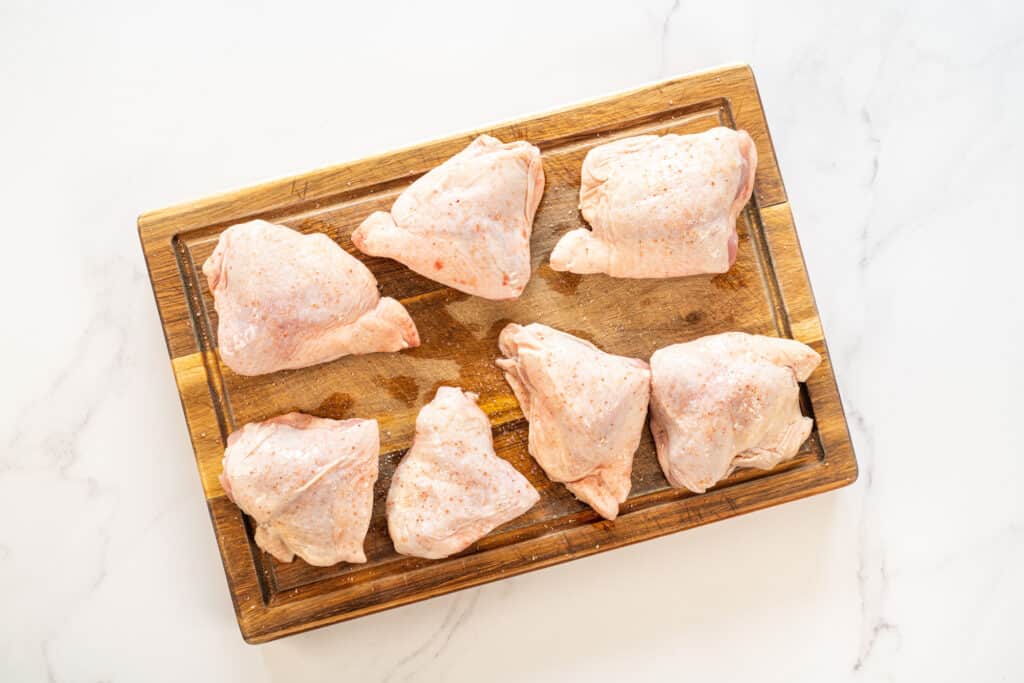 Top view of cutting board with seven raw chicken thighs